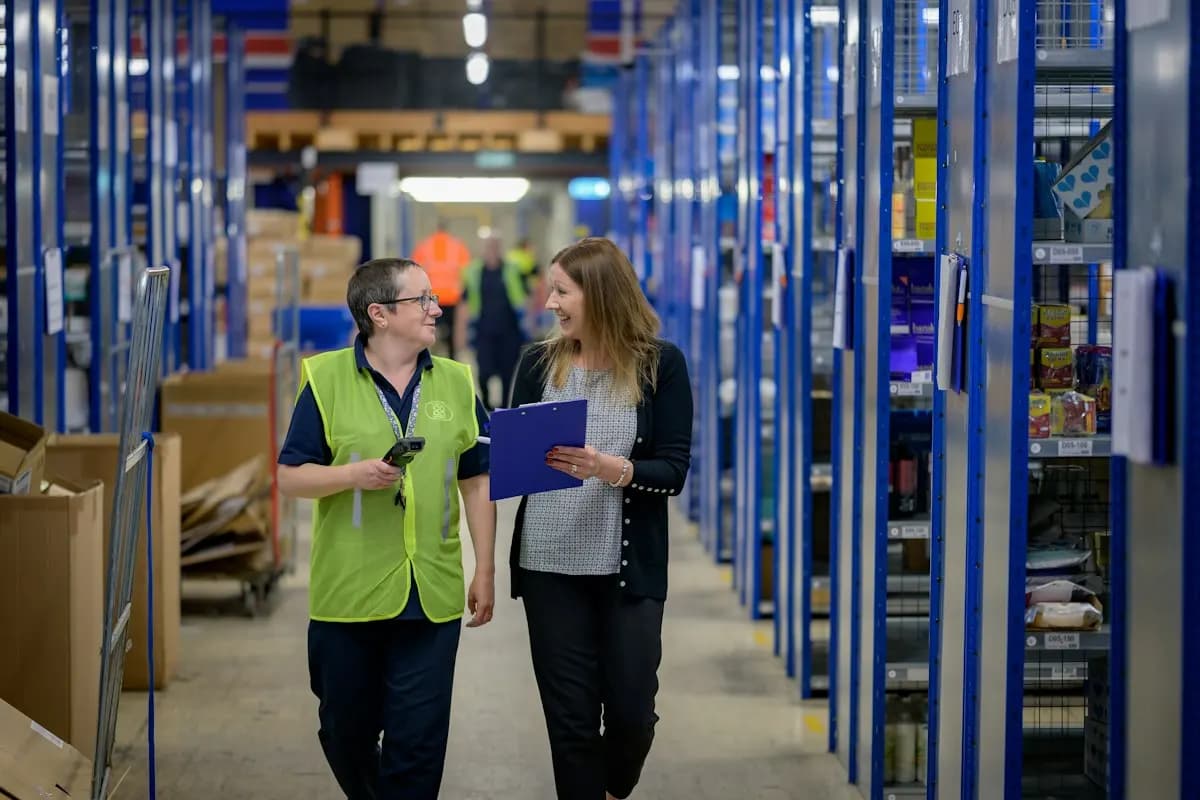 Warehouse staff reviewing logistics operations with a clipboard and scanner between shelving aisles